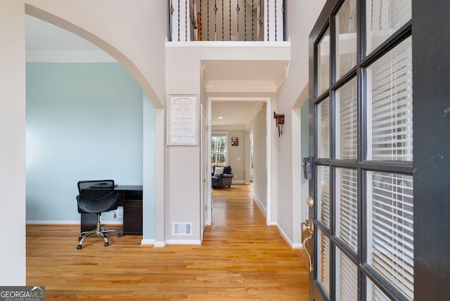 interior space with a high ceiling, ornamental molding, and light hardwood / wood-style flooring