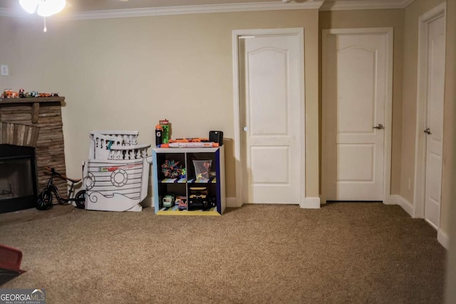 rec room with ornamental molding, a stone fireplace, and carpet flooring