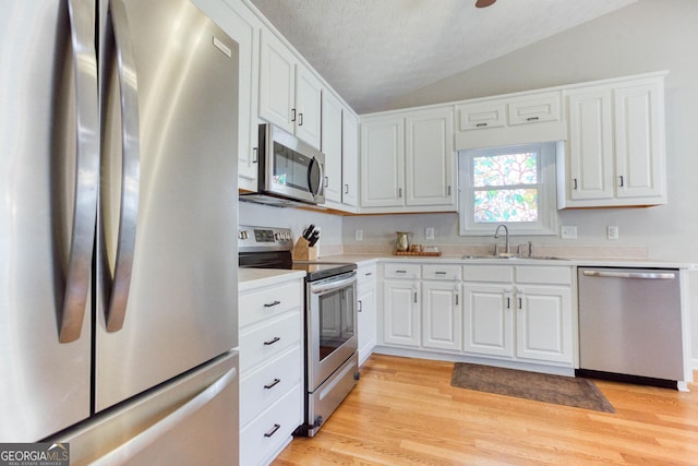 kitchen featuring sink, vaulted ceiling, light wood-type flooring, appliances with stainless steel finishes, and white cabinets