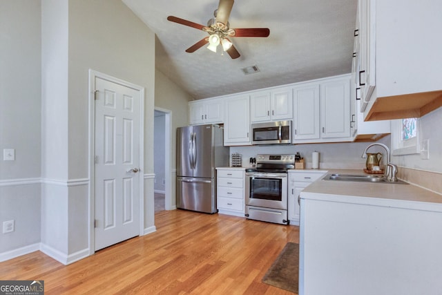 kitchen featuring sink, white cabinetry, vaulted ceiling, light hardwood / wood-style flooring, and stainless steel appliances