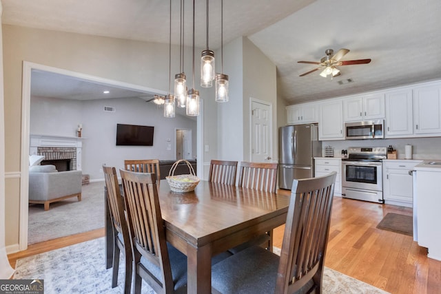 dining room with lofted ceiling, light wood-type flooring, ceiling fan, a brick fireplace, and a textured ceiling