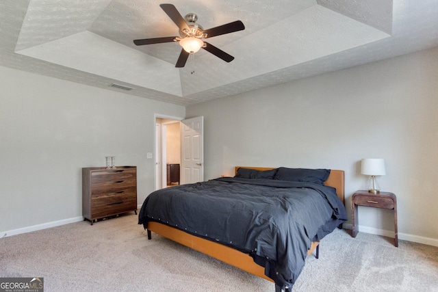 bedroom featuring a raised ceiling, light colored carpet, a textured ceiling, and ceiling fan