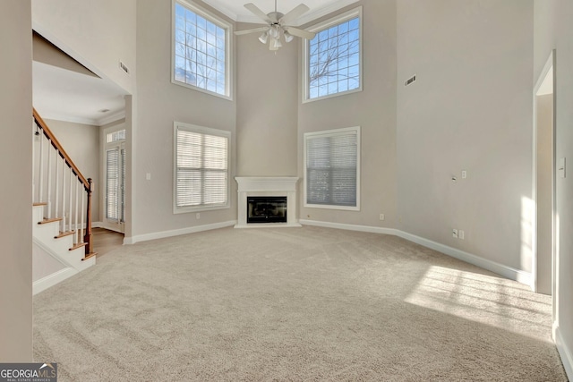 unfurnished living room with ceiling fan, a towering ceiling, ornamental molding, and carpet