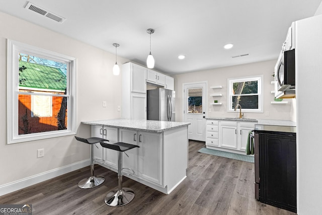 kitchen featuring decorative light fixtures, appliances with stainless steel finishes, kitchen peninsula, light stone countertops, and white cabinets