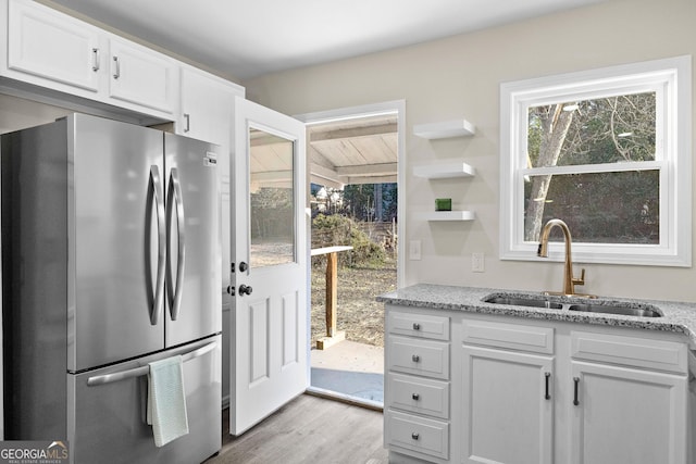 kitchen with white cabinetry, stainless steel fridge, sink, and light stone counters