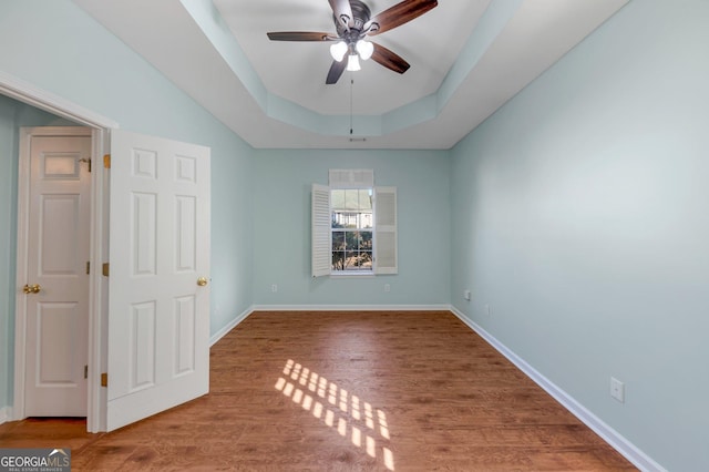 empty room with hardwood / wood-style flooring, ceiling fan, and a raised ceiling