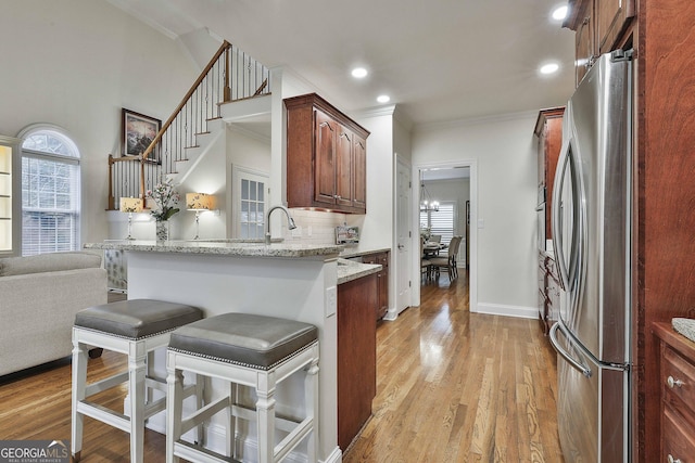 kitchen with stainless steel refrigerator, a breakfast bar, light stone counters, light hardwood / wood-style floors, and kitchen peninsula