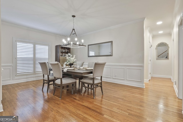 dining space with crown molding, an inviting chandelier, and light wood-type flooring