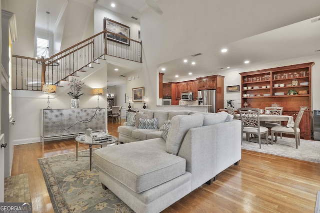 living room featuring a high ceiling, ornamental molding, and light hardwood / wood-style flooring