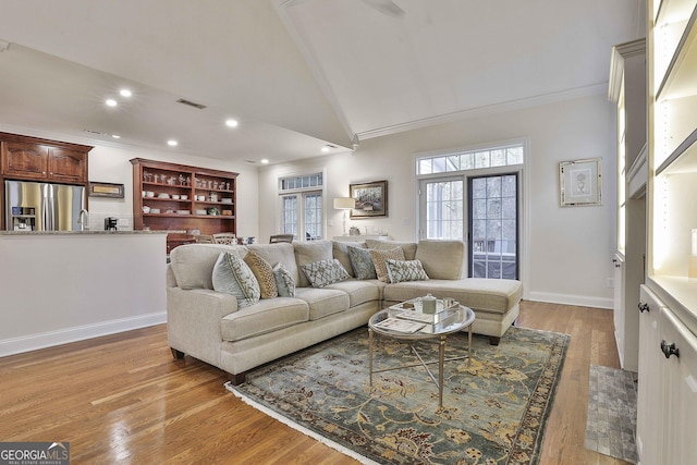 living room featuring ornamental molding, vaulted ceiling, and light wood-type flooring