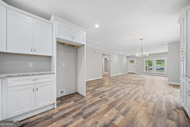 kitchen featuring white cabinetry, light stone counters, wood-type flooring, and an inviting chandelier