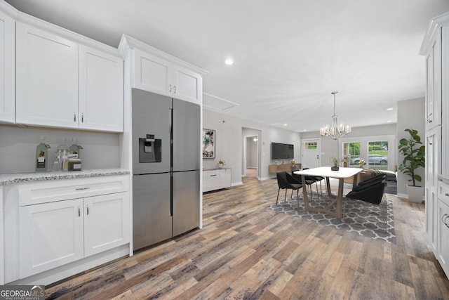 kitchen featuring white cabinets, wood-type flooring, light stone countertops, and stainless steel fridge