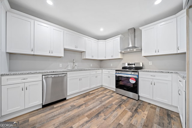 kitchen with white cabinetry, appliances with stainless steel finishes, sink, and wall chimney range hood