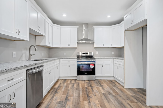 kitchen with white cabinetry, stainless steel appliances, sink, and wall chimney range hood