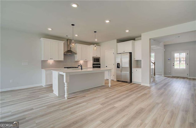 kitchen with white cabinetry, appliances with stainless steel finishes, a kitchen island with sink, and wall chimney exhaust hood