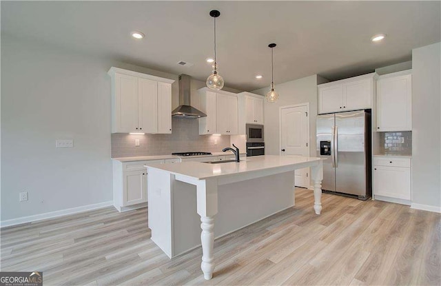 kitchen featuring wall chimney exhaust hood, sink, white cabinetry, a center island with sink, and stainless steel appliances