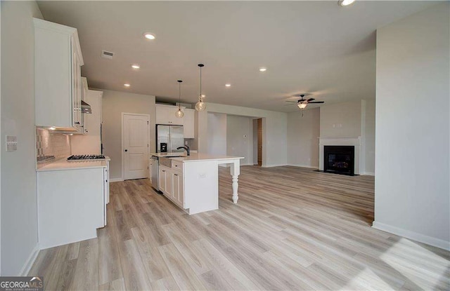 kitchen with decorative light fixtures, white cabinetry, an island with sink, stainless steel appliances, and light wood-type flooring