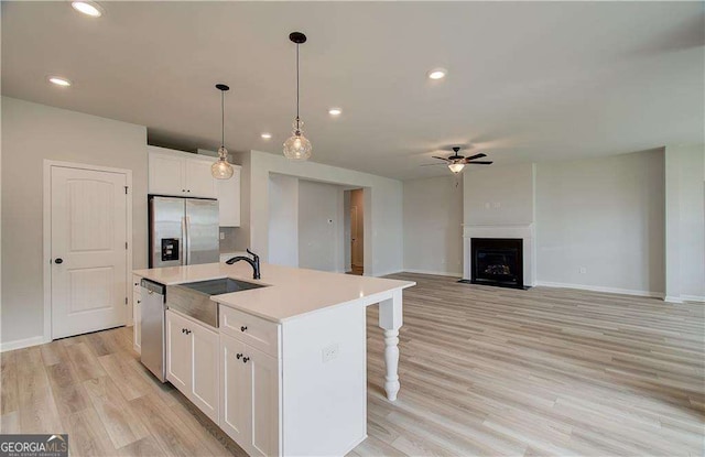 kitchen featuring appliances with stainless steel finishes, pendant lighting, white cabinetry, sink, and a kitchen island with sink