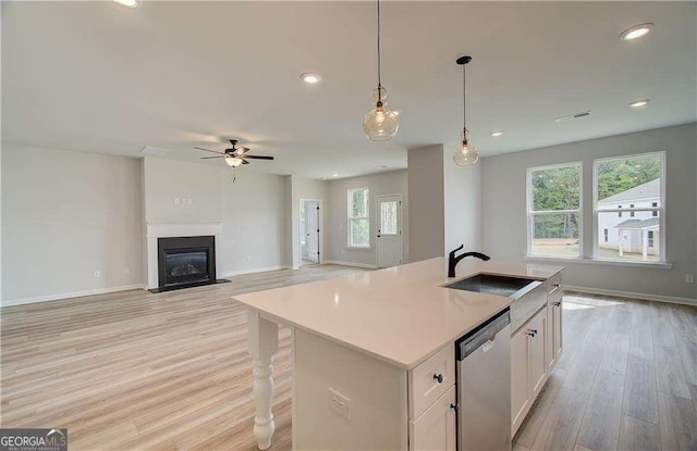 kitchen with sink, dishwasher, a kitchen island with sink, hanging light fixtures, and white cabinets