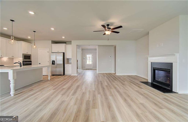 unfurnished living room with sink, light hardwood / wood-style floors, and ceiling fan