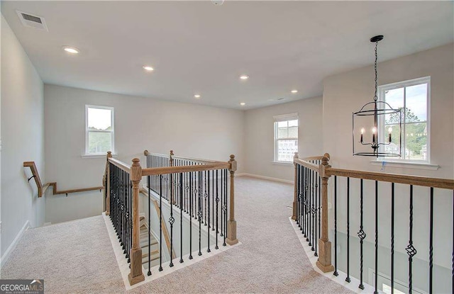 corridor featuring light colored carpet and a notable chandelier