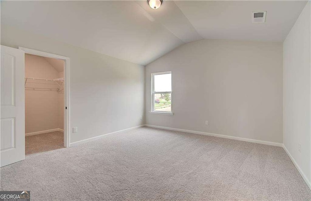 unfurnished bedroom with lofted ceiling, a spacious closet, light colored carpet, and a closet