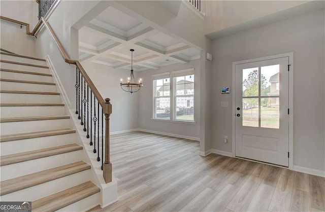 foyer entrance with beam ceiling, coffered ceiling, an inviting chandelier, and light wood-type flooring