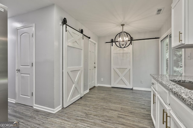 interior space featuring an inviting chandelier, pendant lighting, a barn door, light stone countertops, and white cabinets