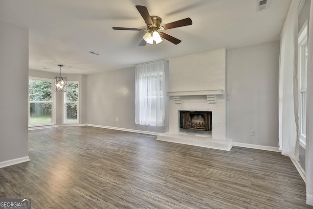 unfurnished living room with dark hardwood / wood-style flooring, ceiling fan with notable chandelier, and a fireplace