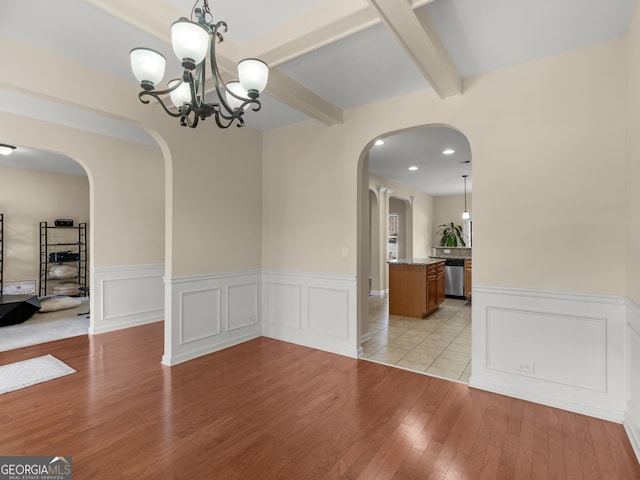 unfurnished dining area with beam ceiling, a notable chandelier, and light wood-type flooring