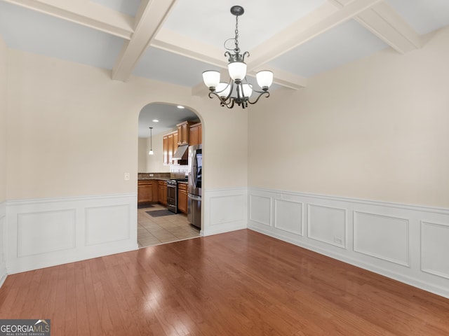 unfurnished dining area featuring an inviting chandelier, beam ceiling, and light hardwood / wood-style floors