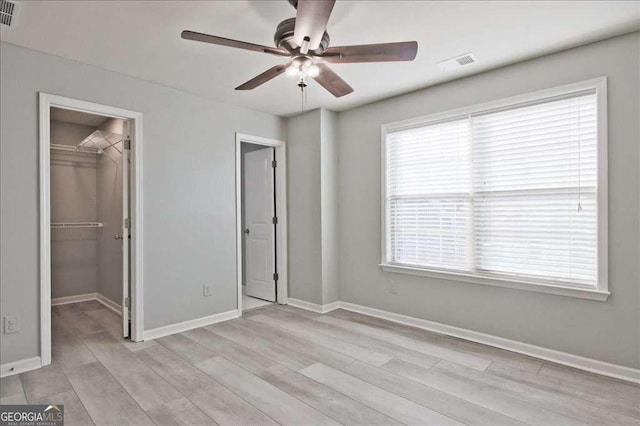 unfurnished bedroom featuring multiple windows, a spacious closet, a closet, and ceiling fan