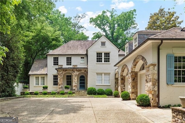 french country home featuring concrete driveway, stone siding, and covered porch