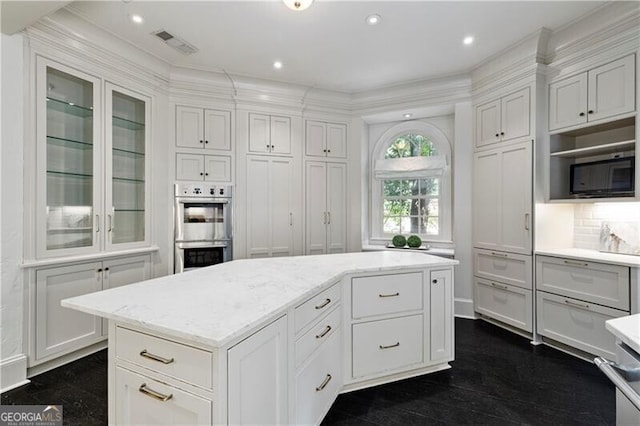 kitchen with a kitchen island, built in microwave, white cabinetry, backsplash, and stainless steel double oven