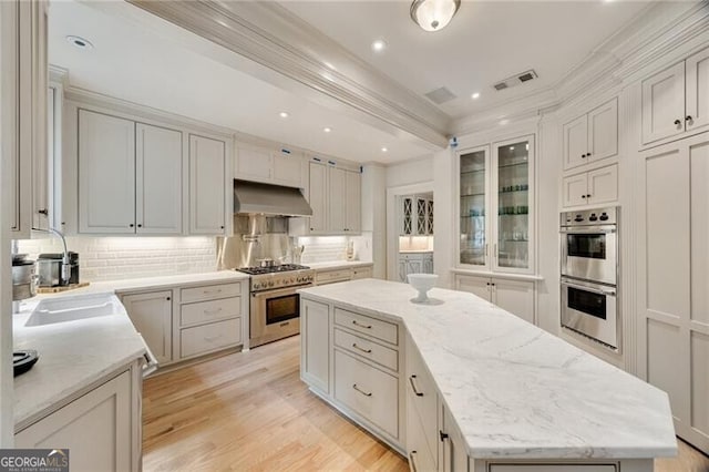 kitchen featuring under cabinet range hood, a center island, visible vents, ornamental molding, and appliances with stainless steel finishes