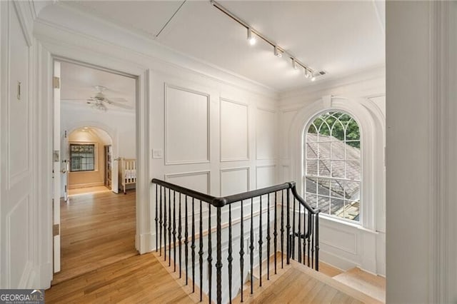 stairway featuring arched walkways, rail lighting, wood finished floors, and a decorative wall