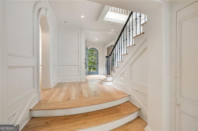 foyer with stairway, a decorative wall, arched walkways, recessed lighting, and wood finished floors