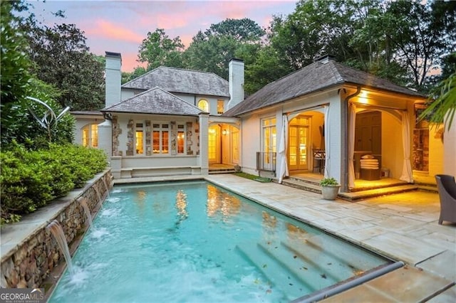 back house at dusk with a patio, an outbuilding, and pool water feature