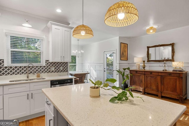 kitchen with light stone counters, decorative light fixtures, sink, and white cabinets