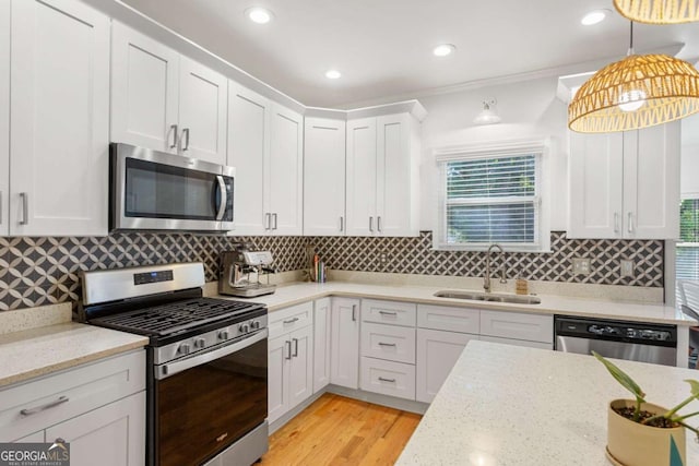 kitchen with white cabinetry, sink, hanging light fixtures, stainless steel appliances, and light stone countertops