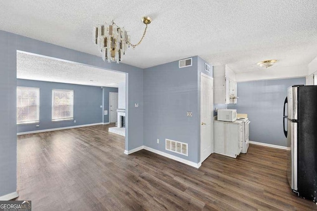 unfurnished dining area featuring dark wood-type flooring, a chandelier, and a textured ceiling