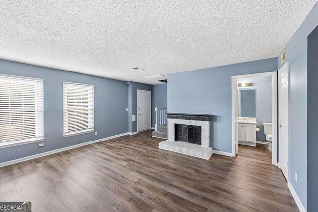 unfurnished living room featuring dark hardwood / wood-style flooring, a brick fireplace, and a textured ceiling