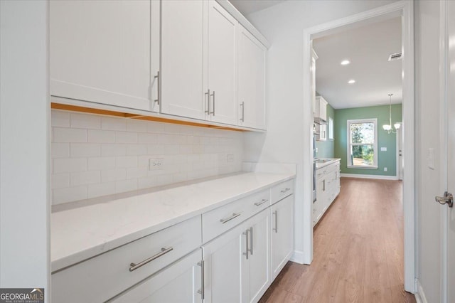 bar featuring white cabinetry, hanging light fixtures, tasteful backsplash, light stone countertops, and light hardwood / wood-style floors