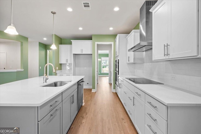 kitchen with sink, wall chimney range hood, stainless steel appliances, white cabinets, and decorative light fixtures