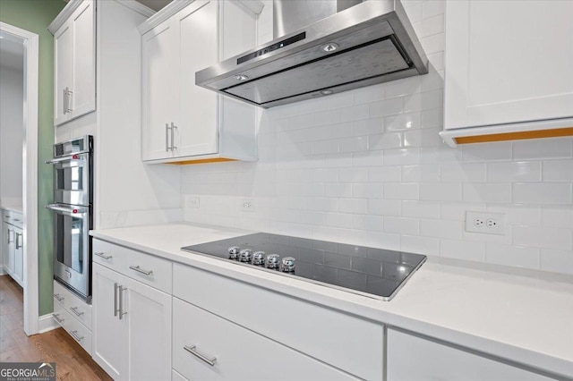 kitchen featuring double oven, white cabinetry, dark hardwood / wood-style flooring, black electric cooktop, and wall chimney exhaust hood