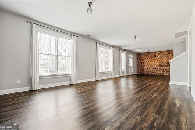 unfurnished living room featuring brick wall, baseboards, and dark wood-type flooring