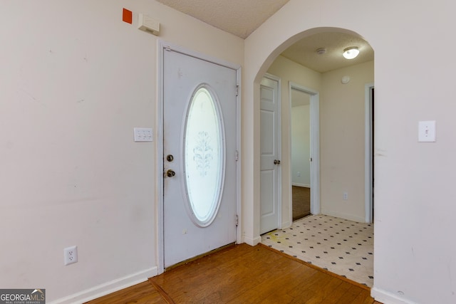 foyer entrance featuring arched walkways, a textured ceiling, wood finished floors, and baseboards