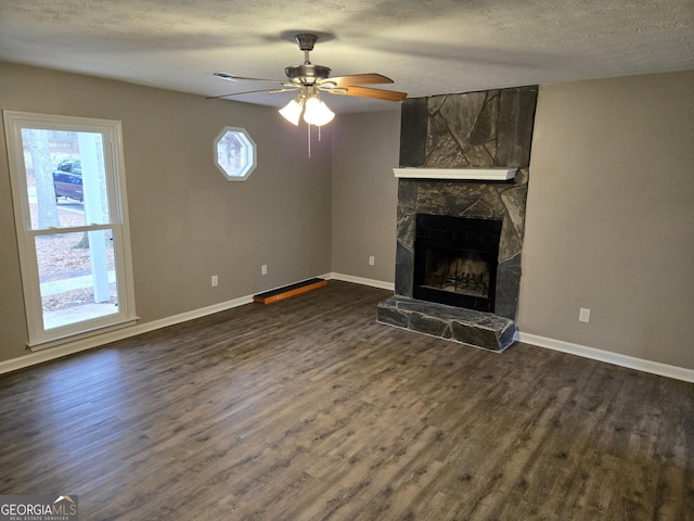 unfurnished living room featuring ceiling fan, a stone fireplace, dark hardwood / wood-style flooring, and a textured ceiling