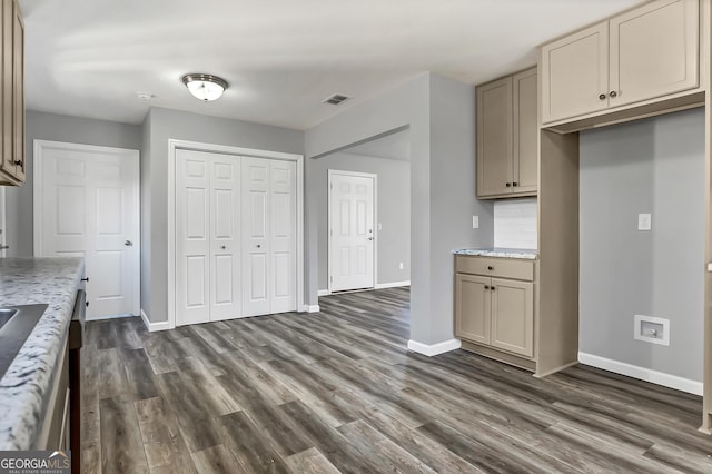 kitchen with light stone counters, cream cabinets, dark wood-type flooring, and decorative backsplash