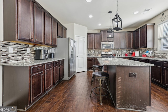 kitchen with dark brown cabinets, stainless steel appliances, a center island, light stone countertops, and dark hardwood / wood-style flooring